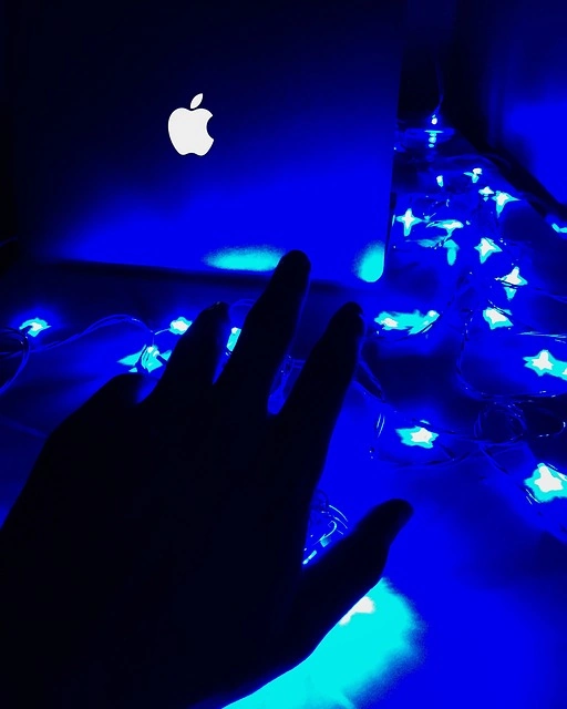 A person holding an apple laptop with blue lights on it.