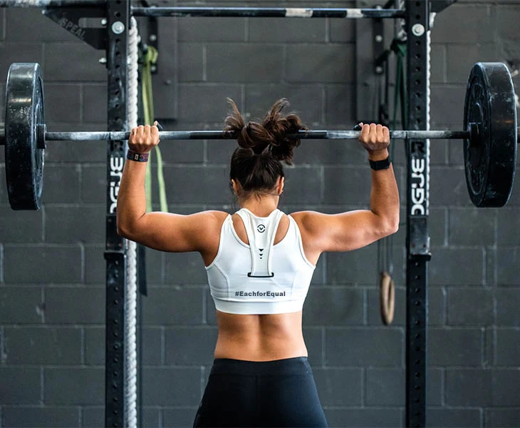 A woman lifting a barbell in a gym.