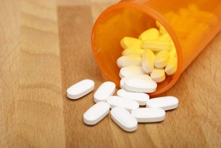 A pill bottle with pills spilling out on a wooden table.