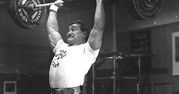 An old photo of a man lifting a barbell.