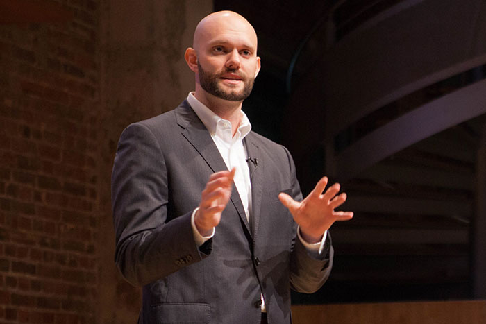 A bald man in a suit standing in front of a brick wall.