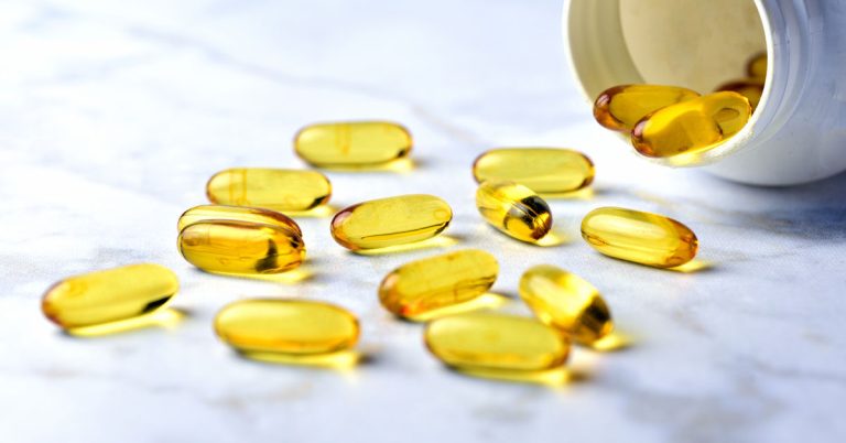 Some fish oil capsules are falling out of a bowl.