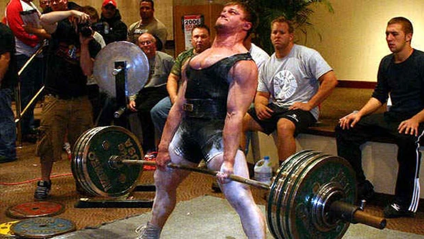 A man lifting a barbell in front of a crowd.