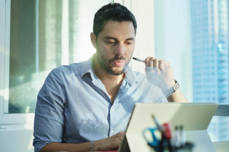 A man smoking a cigarette while working on his laptop.