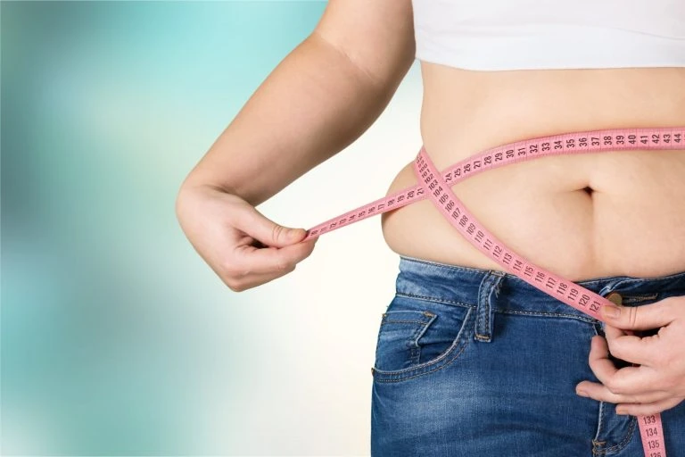 A woman is measuring her waist with a measuring tape.