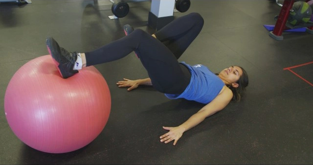 A woman laying on an exercise ball in a gym.