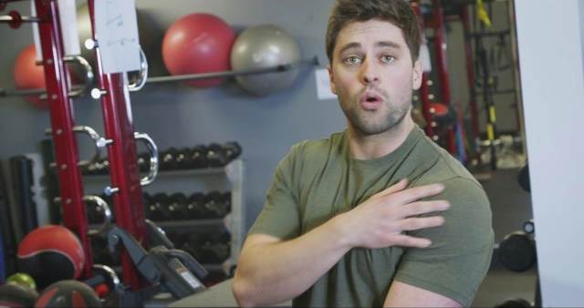 A man standing in a gym with weights in front of him.