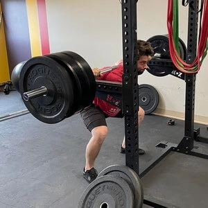 A man squatting with a barbell in a gym.